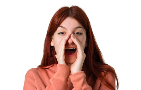 Young redhead girl with pink sweatshirt shouting with mouth wide open and announcing something on isolated white backgroundの写真素材
