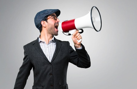 Handsome modern man with beret and glasses holding a megaphone on grey backgroundの写真素材