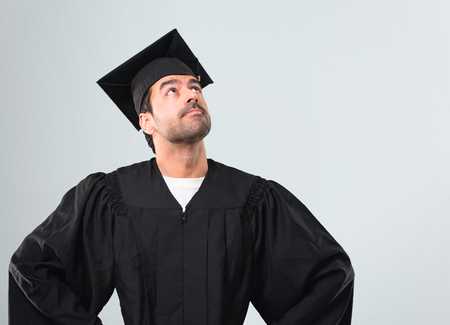 Man on his graduation day University stand and looking up on grey backgroundの写真素材
