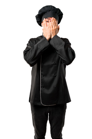 Chef man In black uniform covering eyes by hands and looking through the fingers on isolated white backgroundの写真素材