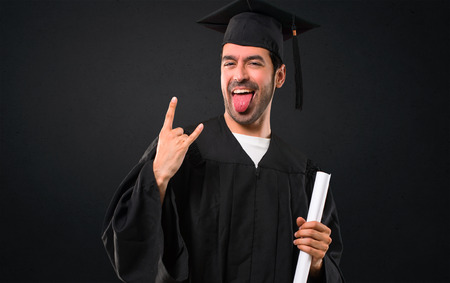 Man on his graduation day University showing tongue at the camera having funny look and taking out the horns on black backgroundの写真素材