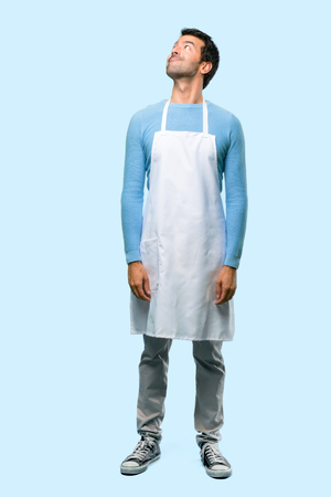 Full body of Man wearing an apron stand and looking up with serious face on blue backgroundの写真素材