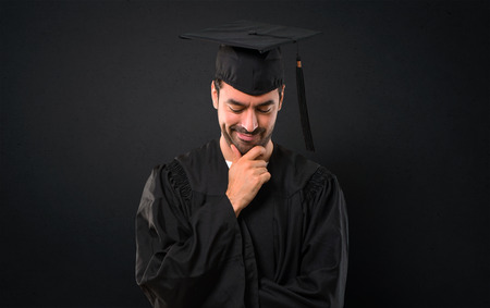 Man on his graduation day University standing and looking down with the hand on the chin on black backgroundの写真素材