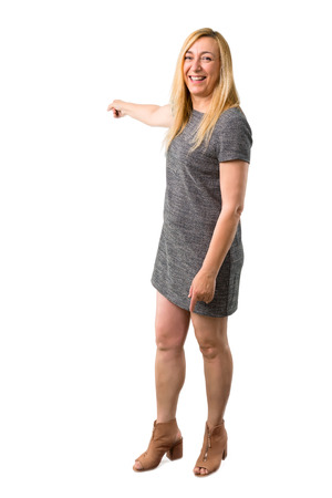 Middle age blonde woman with grey dress pointing back with the index finger presenting a product on isolated white backgroundの写真素材