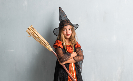 Little girl dressed as a witch and holding a broom for halloween holidays with her arms crossedの写真素材
