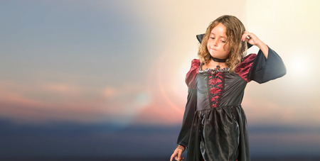 Kid dressed as a vampire at halloween holidays standing and thinking an idea at outdoor with sunsetの写真素材