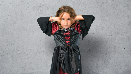 Kid dressed as a vampire at halloween holidays covering both ears with hands on textured backgroundの写真素材