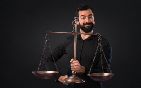 Handsome man with beard holding a balance on black backgroundの写真素材