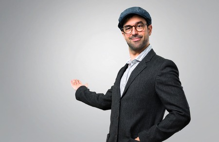 Handsome modern man with beret and glasses pointing back with the index finger on grey backgroundの写真素材