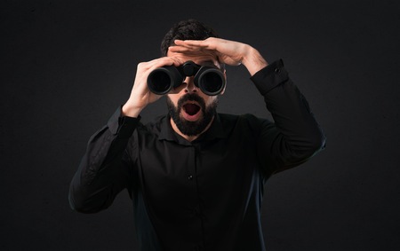 Handsome man with beard with binoculars on black backgroundの写真素材