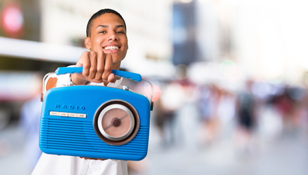 Young african american man with white shirt holding a blue vintage radio in the middle of the cityの写真素材