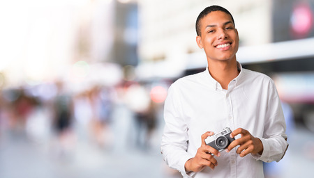 Young african american man with white shirt holding a camera in the middle of the cityの写真素材