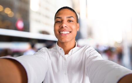 Happy young african american man  taking a selfie with the mobile in the middle of the cityの写真素材