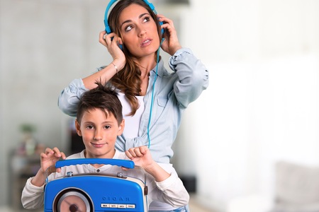 Mother and daughter listening to music with headphones and radio inside houseの写真素材