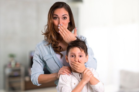 Mother and daughter covering mouth with hands inside houseの写真素材