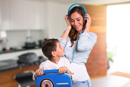 Mother and daughter listening to music with headphones and radio inside houseの写真素材