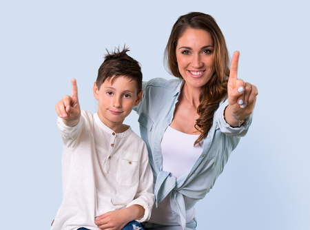 Mother and daughter counting number one sign on blue backgroundの写真素材