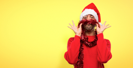 Man with red clothes celebrating the Christmas holidays makes funny and crazy face emotion on yellow backgroundの写真素材