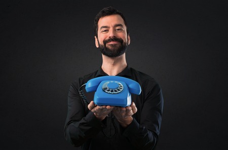 Handsome man with beard talking to vintage phone on black background