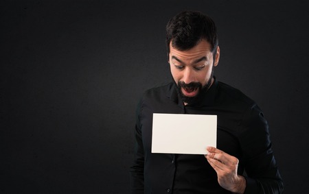 Handsome man with beard holding an empty placard on black backgroundの写真素材