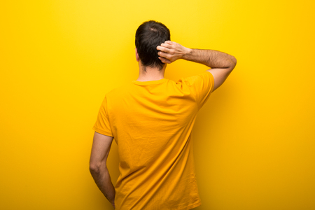 Man on isolated vibrant yellow color on back position looking back while scratching headの写真素材