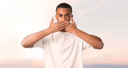 Young african american man covering mouth with hands for saying something inappropriate. Can not...