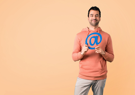 Man in a pink sweatshirt holding icon of at dot com on ocher backgroundの写真素材