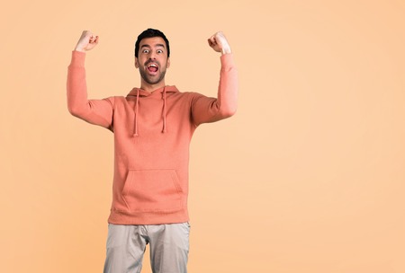 Man in a pink sweatshirt celebrating a victory and happy for having won a prize on ocher background