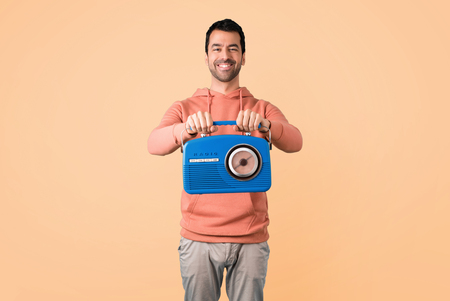 Man in a pink sweatshirt holding a blue vintage radio on ocher backgroundの写真素材