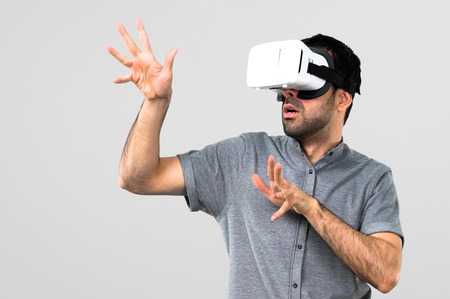 Handsome man using VR glasses on grey background
