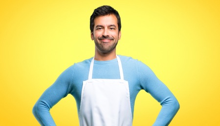 Man wearing an apron posing with arms at hip and laughing looking to the front on yellow backgroundの写真素材