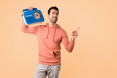 Man in a pink sweatshirt holding a blue vintage radio on ocher backgroundの写真素材
