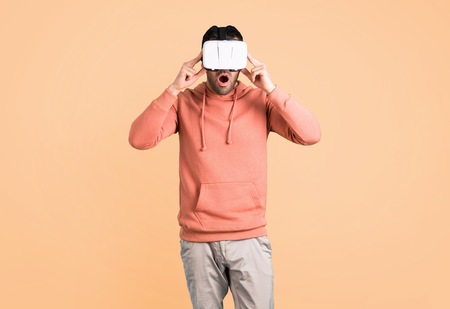 Man in a pink sweatshirt using VR glasses. Virtual reality experience on ocher background