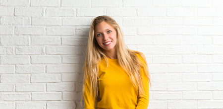 Happy blonde young girl on white brick wall backgroundの写真素材