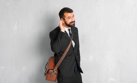 Businessman with beard listening to something by putting hand on the earの写真素材