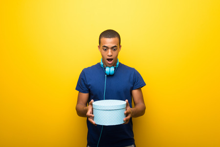 African american man with blue t-shirt on yellow background holding gift boxes in hands