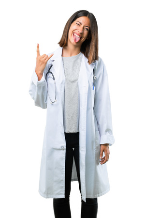 Doctor woman with stethoscope showing tongue at the camera having funny look and taking out the horns on isolated white backgroundの写真素材