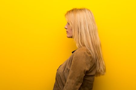 Blonde girl on vibrant yellow background in lateral positionの写真素材