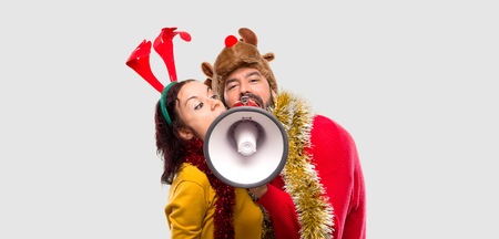 Couple dressed up for the christmas holidays holding a megaphone on isolated background