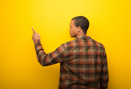 Young african american man on vibrant yellow background pointing back with the index fingerの写真素材
