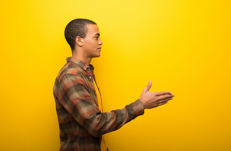 Young african american man on vibrant yellow background handshaking after good dealの写真素材
