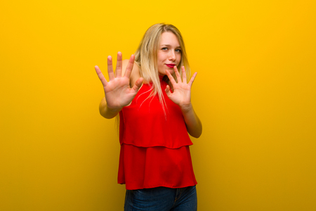 Young girl with red dress over yellow wall is a little bit nervous and scared stretching hands to the frontの写真素材