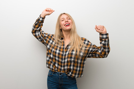 Blonde young girl over white wall celebrating a victoryの写真素材