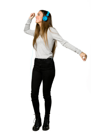 Full-length shot of young girl listening to music with headphones and dancing on isolated white backgroundの写真素材