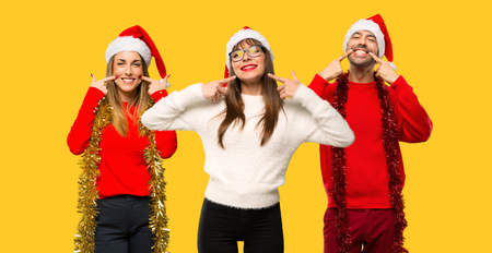 A group of people Blonde woman dressed up for christmas holidays smiling with a pleasant expression while pointing mouth with fingers on yellow backgroundの写真素材