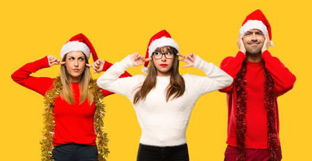 A group of people Blonde woman dressed up for christmas holidays covering ears with hands on yellow backgroundの写真素材