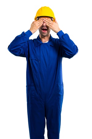 Young workman with helmet covering eyes by hands. Surprised to see what is ahead on isolated white backgroundの写真素材