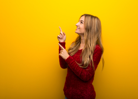 Young girl on vibrant yellow background pointing with the index finger and looking upの写真素材