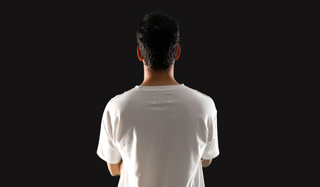 Young man with white shirt in back position on isolated black backgroundの写真素材