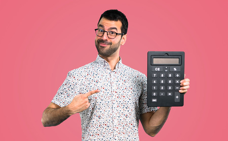 Handsome man with glasses holding a calculator on pink backgroundの写真素材